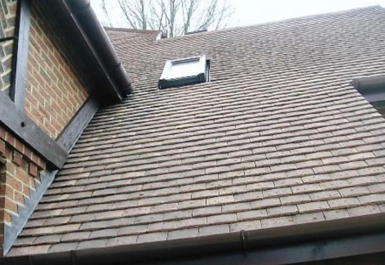 Close-up of residential roof with gray shingles, brick chimney, and a skylight window