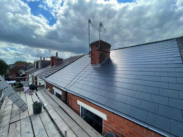 Slate blue roof with red brick chimney against cloudy sky, renovation work in progress