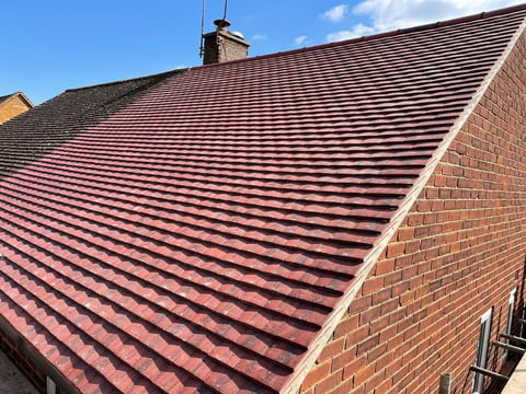 Red clay tile roof on brick building with chimney under clear blue sky