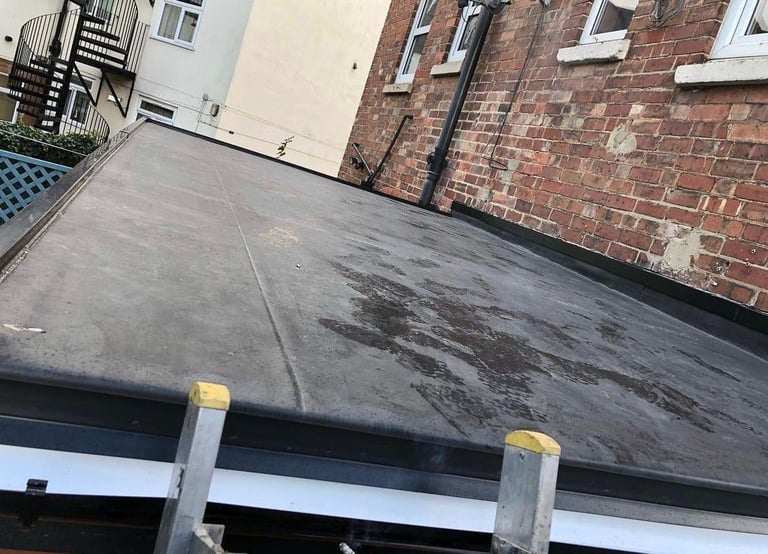 Flat asphalt roof with wet surface between brick building and white building with metal fire escape