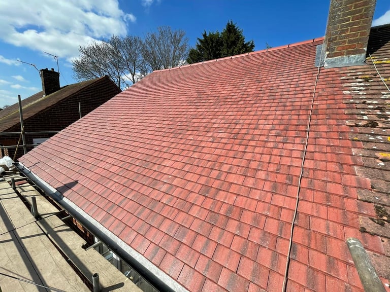 Newly installed red clay tile roof on a residential house with clear blue sky and trees in background