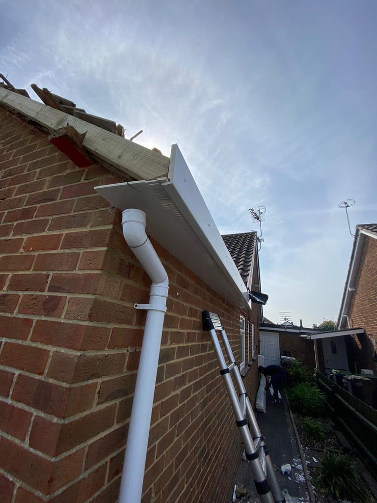 White downspout and gutter on red brick house exterior with residential street and other homes visible