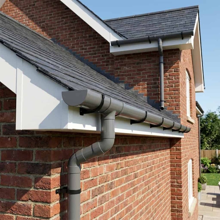 Gray metal gutter and downpipe system installed on brick house exterior under clear blue sky