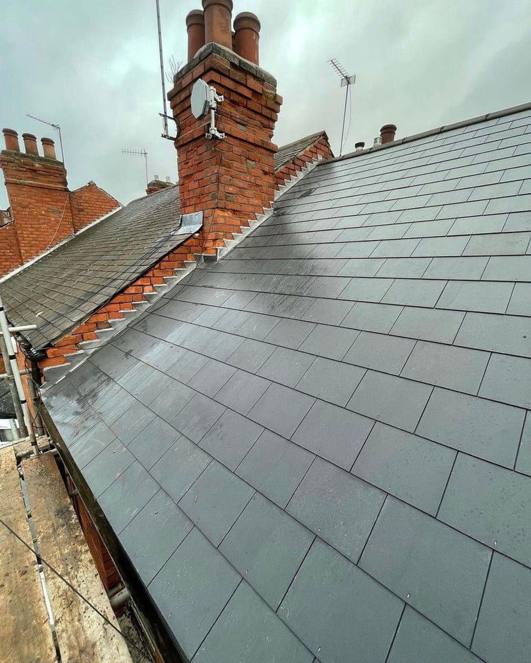 Slate roof with multiple red brick chimneys on a residential building against an overcast sky