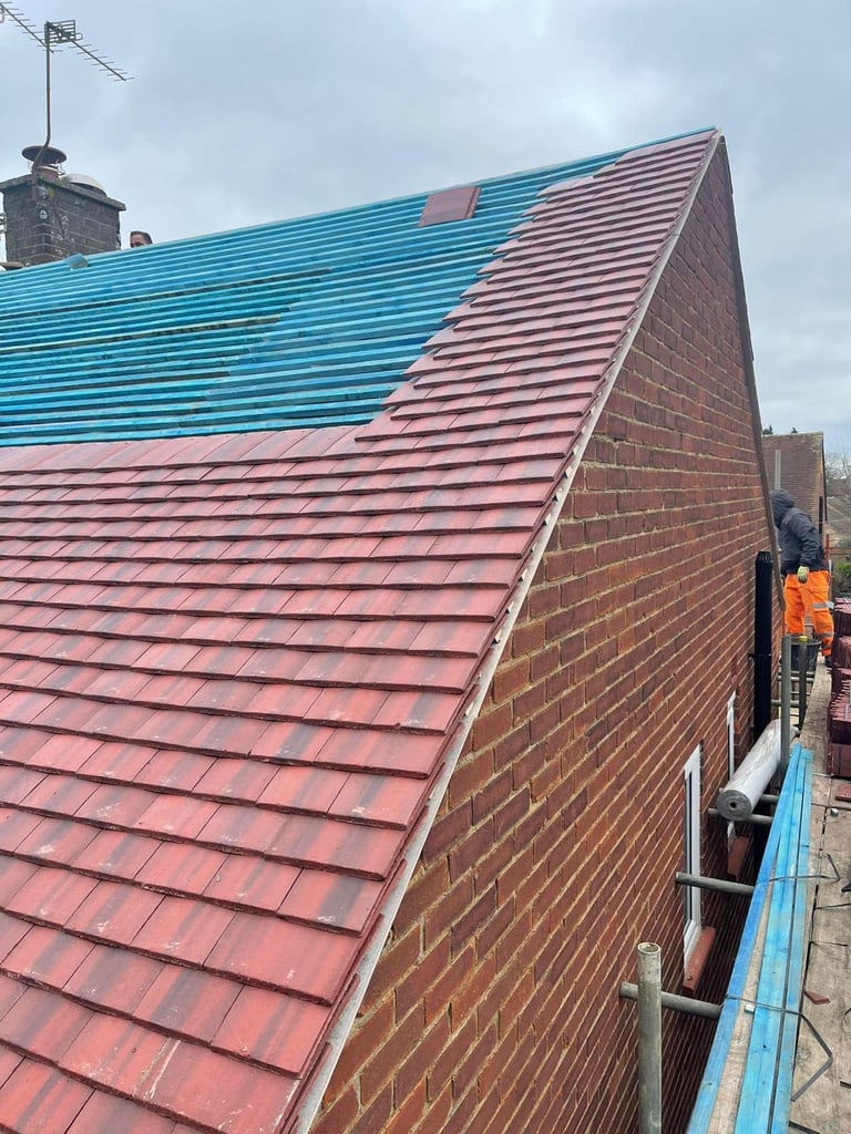 Roofer in orange safety vest working on new pink metal roof installation with turquoise gutter and brick walls