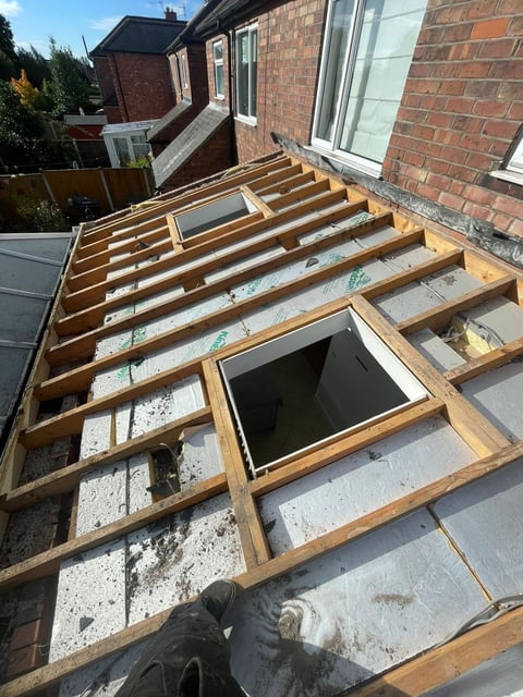 Construction view of wooden roof framing on brick house with exposed joists and skylights during renovation