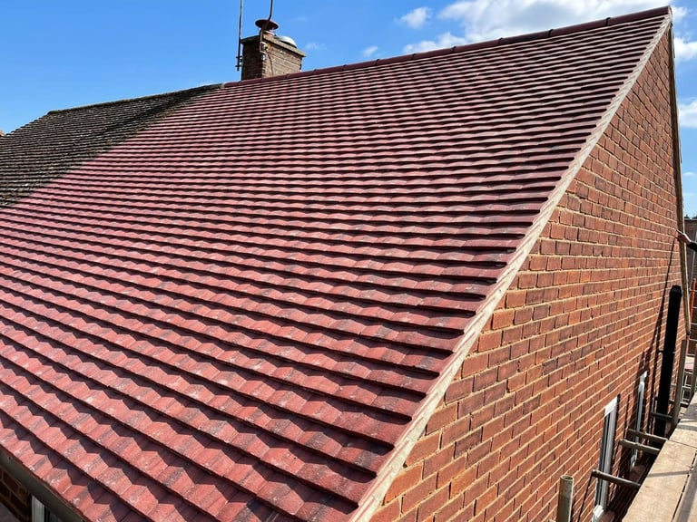 Red tile roof on brick building with blue sky and white clouds in background