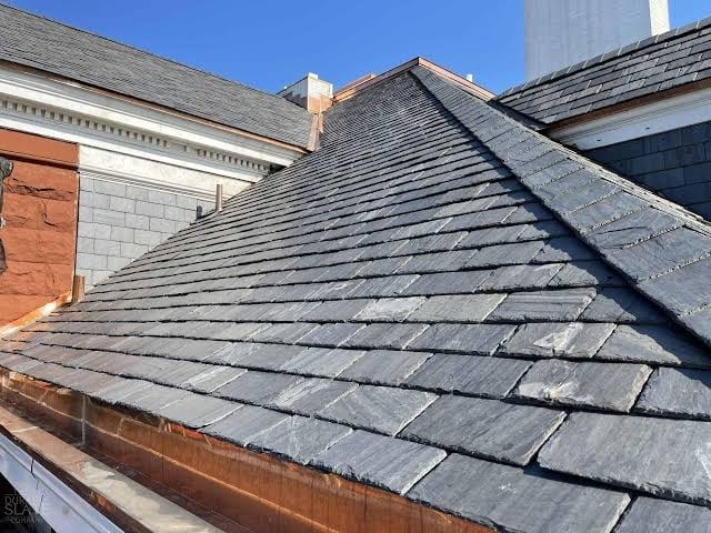 Close-up view of slate roof tiles on pitched roof of brick building under clear blue sky