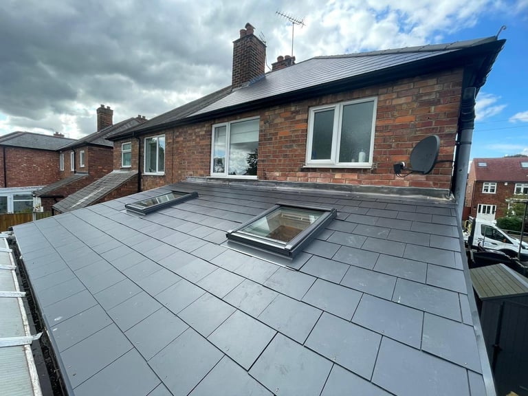 Modern flat roof on brick house with skylights and satellite dish, surrounded by residential buildings