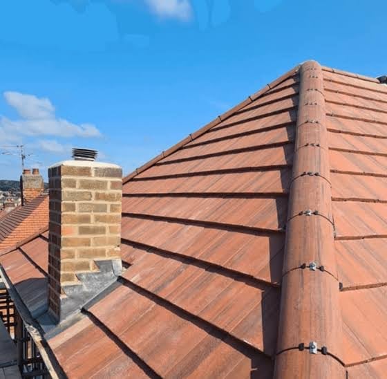 Red clay roof with horizontal tiles, brick chimney, and metal flashing under blue sky