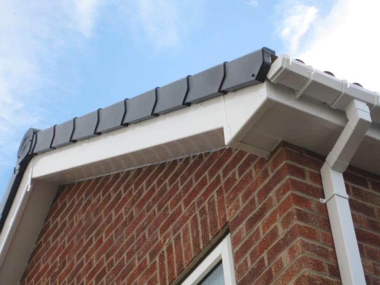 Close-up of a brick building corner showing white gutters and downspout against red brick wall under blue sky
