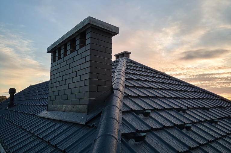 Slate roof with brick chimney against cloudy sky at sunset