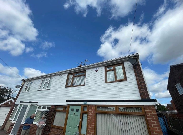 Semi-detached brick and white-rendered house with green door, garage, and blue sky with clouds
