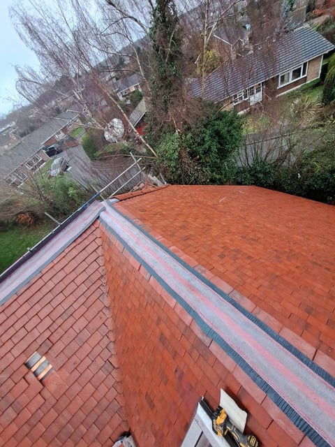 Aerial view of a residential roof with red brick tiles and metal flashing, overlooking a neighborhood with houses and bare trees