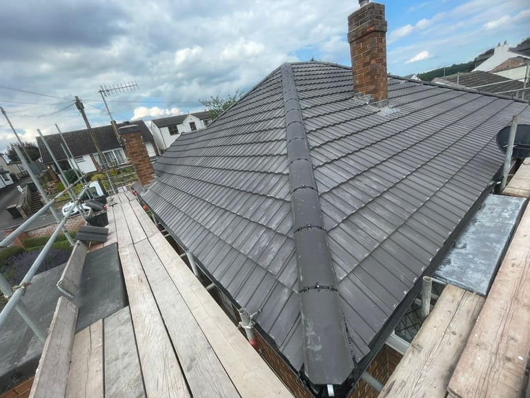 Aerial view of a newly installed dark gray metal roof on a residential building with brick chimney and surrounding construction site