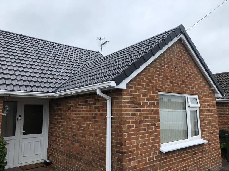 Red brick bungalow with dark tiled roof, white door and window frame, and overcast sky